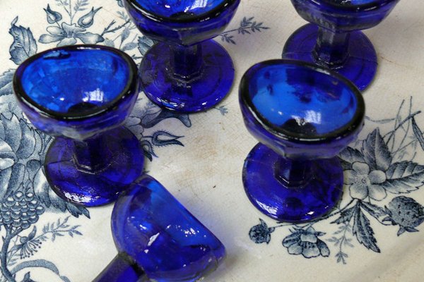Alte blaue Augenbad-Gläser stehen auf einem alten Teller mit Blumenmuster